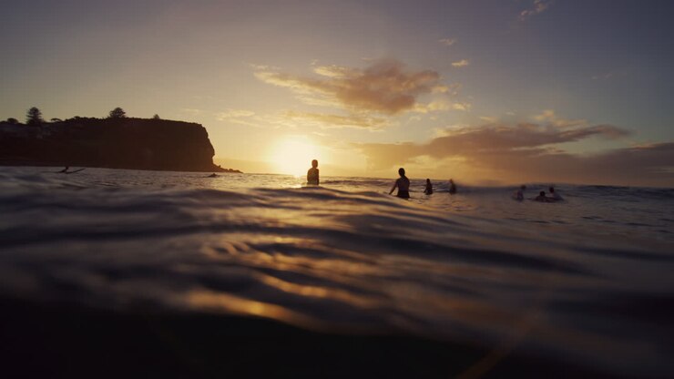 View from ocean water surface as silhouette of surfers wait at break during sunrise