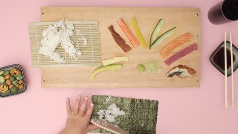 top shot di due mani che preparano il sushi su un tavolo rosa