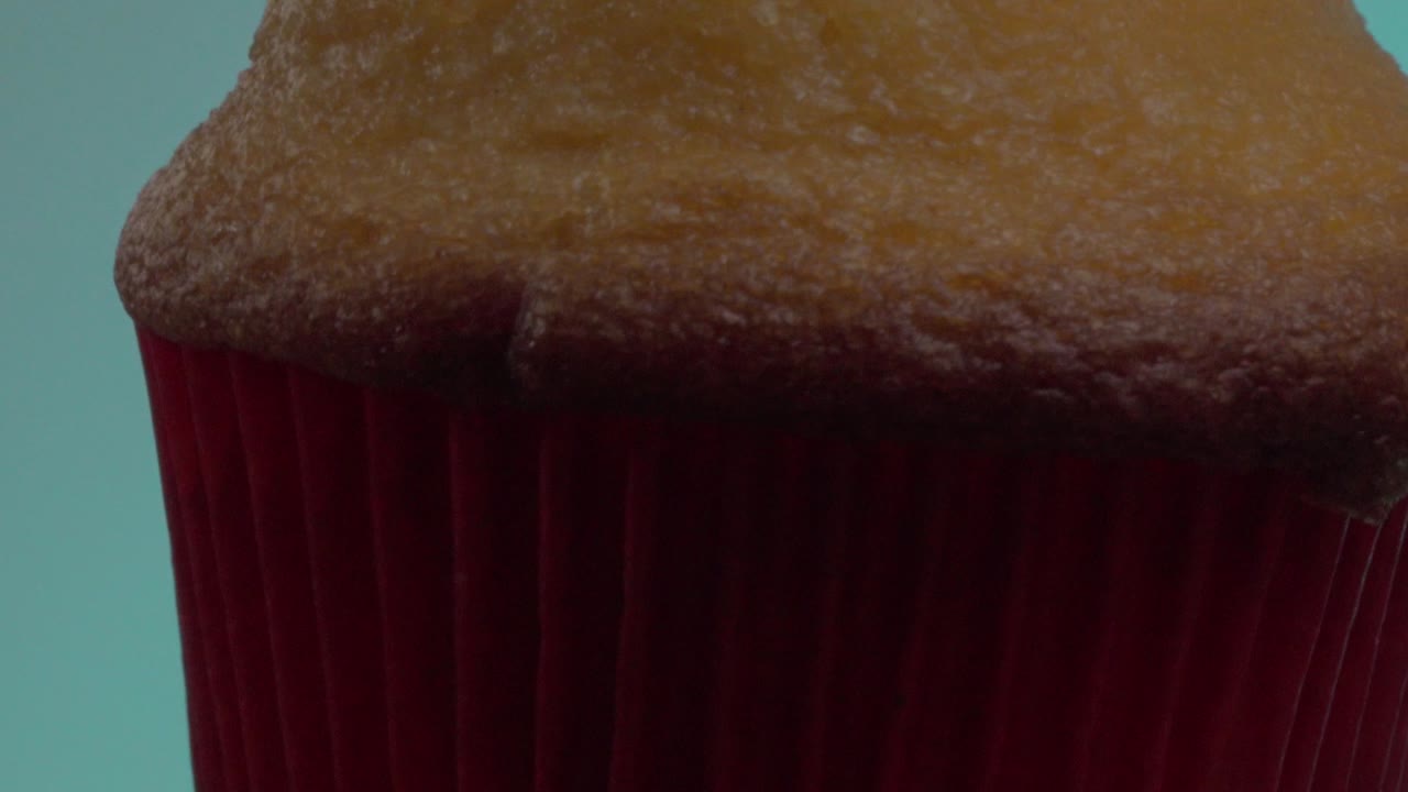 Detailed close-up of a golden muffin in a red wrapper with a light blue background, showcasing its texture