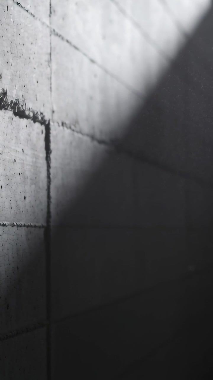Vídeo vertical: Luz mudando, sombra se movendo pela parede de blocos de concreto no corredor, revelando a textura.