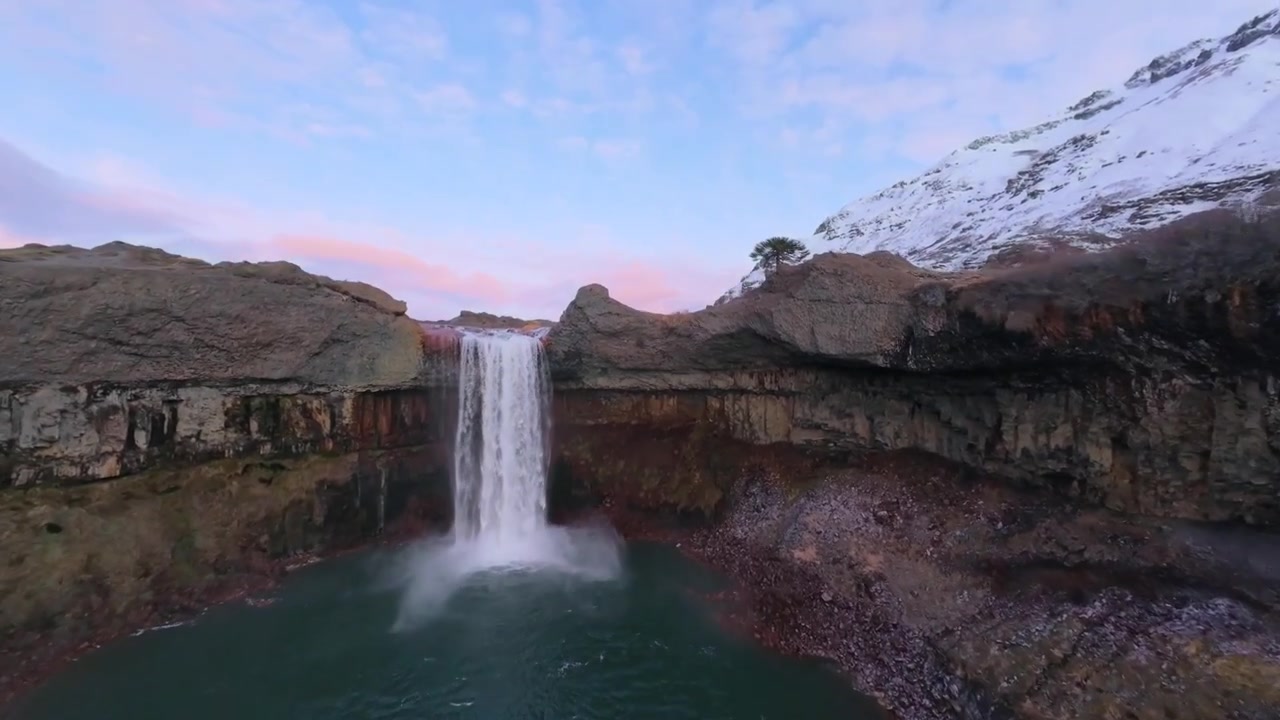 La cascata Salto del Agrio scorre attraverso il canyon vulcanico di Caviahue Copahue, Neuquen, Argentina, rivelando depositi minerali rossi, scogliere di basalto e cime innevate, sorvolo FPV.