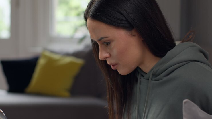 Close Up Of Anxious Woman Sitting Indoors On Sofa Working From Home Using Laptop Worried About Cost Of Living Crisis