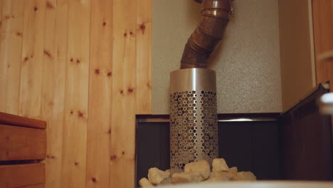 interior view of sauna featuring vertical wooden panel wall with warm natural knots, round ceiling light softly glowing at center, and metal exhaust pipe on right