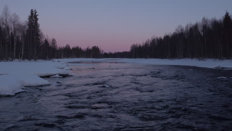 dynamic, cinematic low level aerial shot up an icy river at dusk