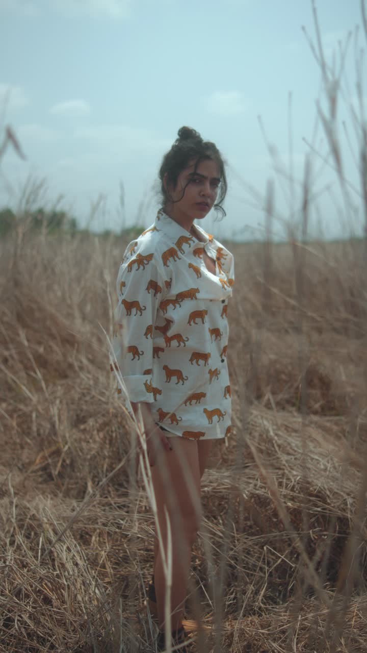 Young woman standing in a field of tall dry grass, wearing a white shirt with a tiger print