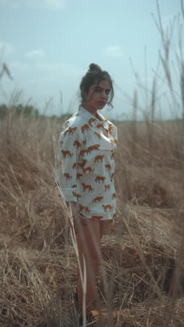 young woman standing in a field of tall dry grass, wearing a white shirt with a tiger print