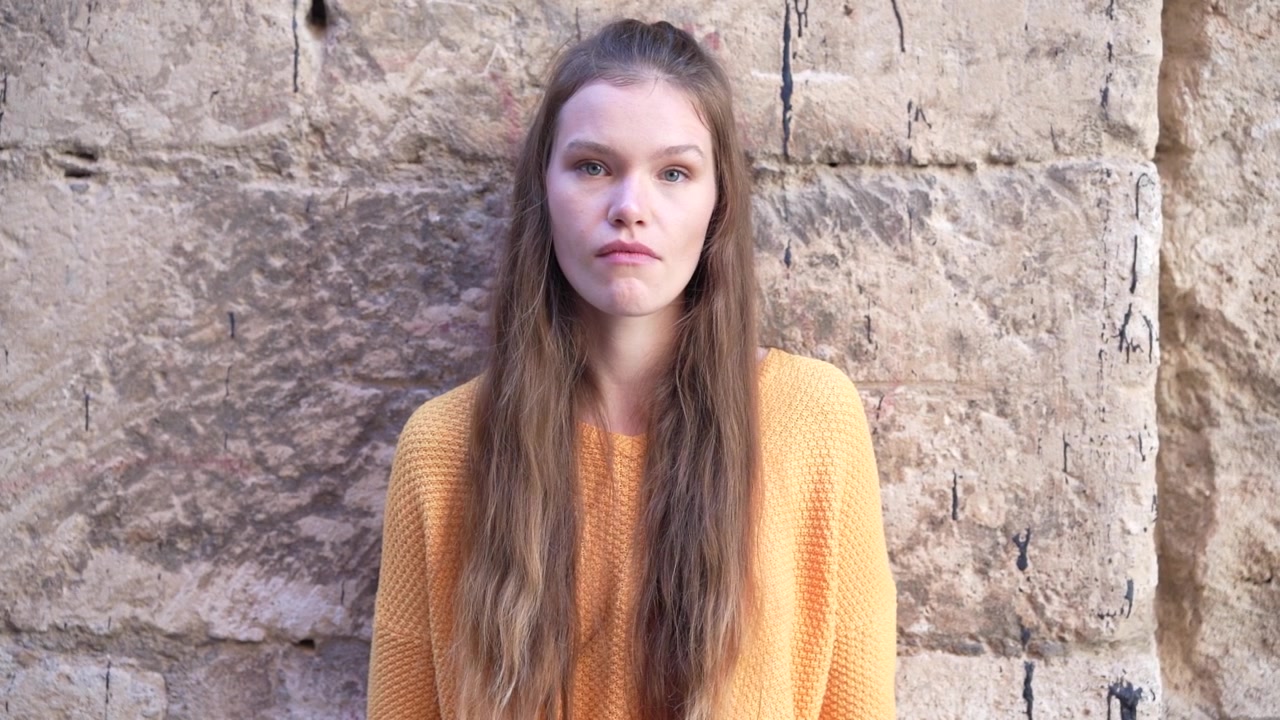 Un bellissimo ritratto di una giovane donna su uno sfondo di muro di pietra texturizzato che trasmette emozione.