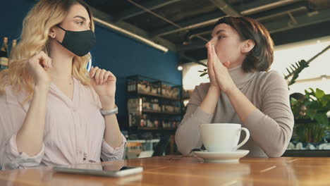 female friends with face mask talking in a coffee shop