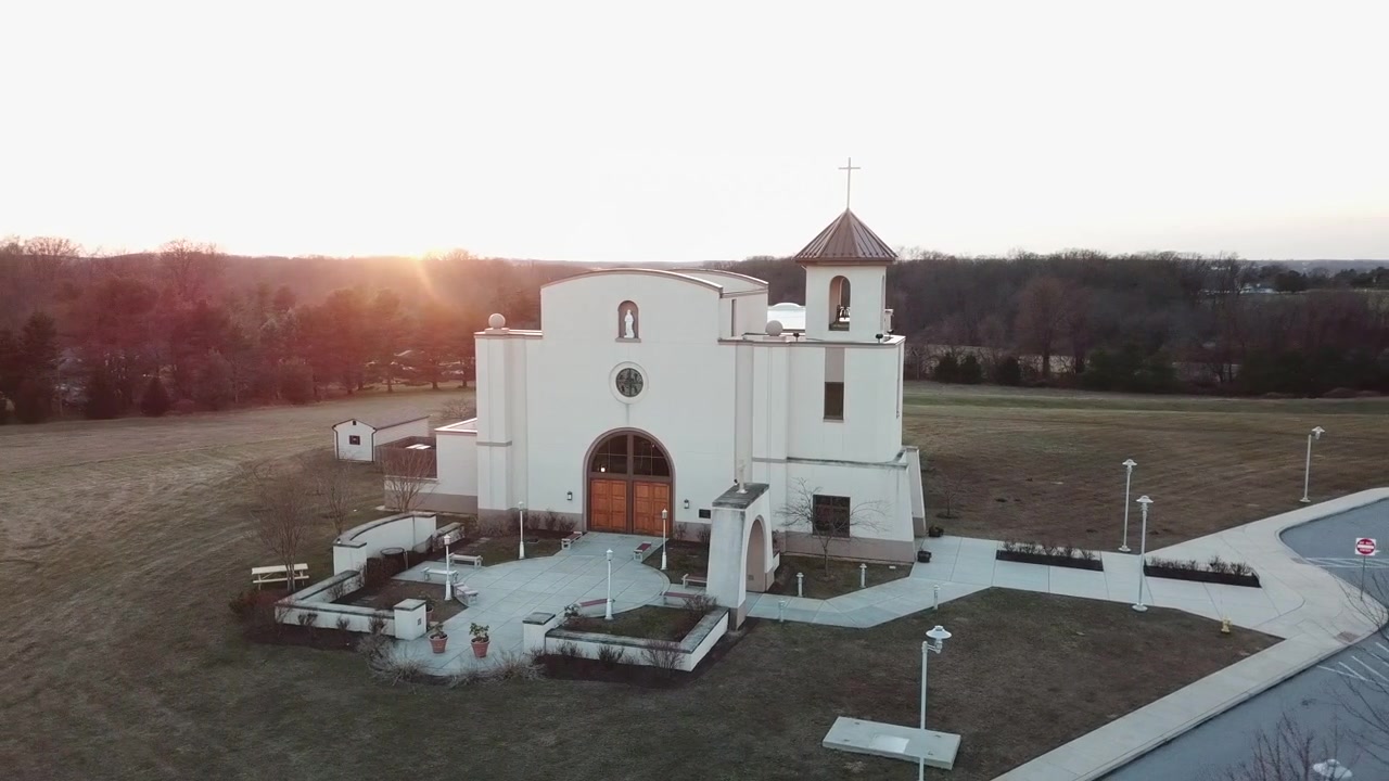 Drone voando baixo com vista frontal de uma igreja e o pôr do sol ao fundo num dia de inverno