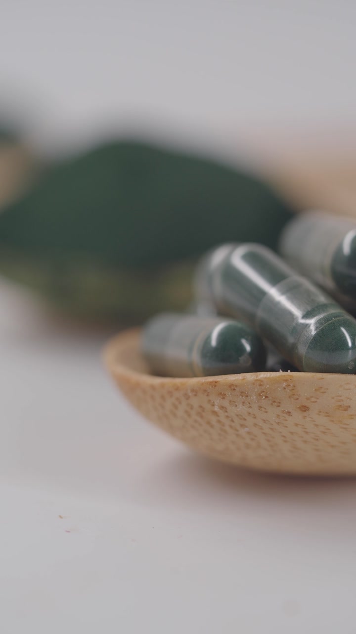 Healthy Green Supplement Capsules in a Wooden Spoon