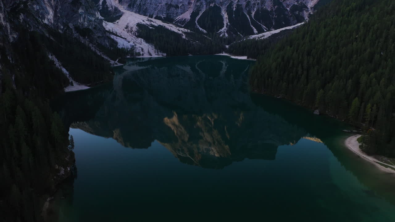 Drone shot tilting over the mirroring lake Pragser Wildsee, in sunny Dolomites, Italy