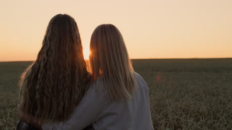 two women admiring the sunset over a field of wheat, rear view