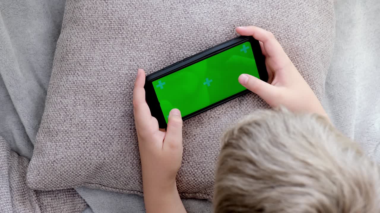 초록색 화면을 가진 스마트폰을 들고 스마트폰에서 모바일 게임을 하는 4k 소년