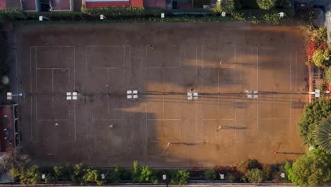 toma de arriba hacia abajo de cinco canchas de tenis de tierra batida con jugadores practicando en la mañana en la ciudad de méxico