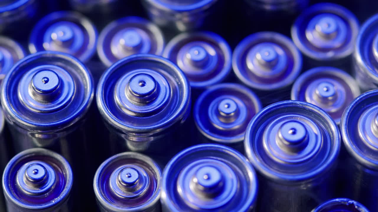 Silver batteries AA and AAA in neon light close-up. Double-A battery is a standard size single cell cylindrical dry battery. Batteries are common in portable electronic devices. An AA battery is composed of a single electrochemical cell that may be either a primary battery or a rechargeable battery.