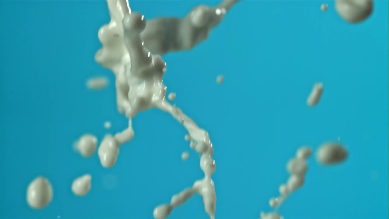Leite branco espirrando em câmera lenta em um fundo azul.