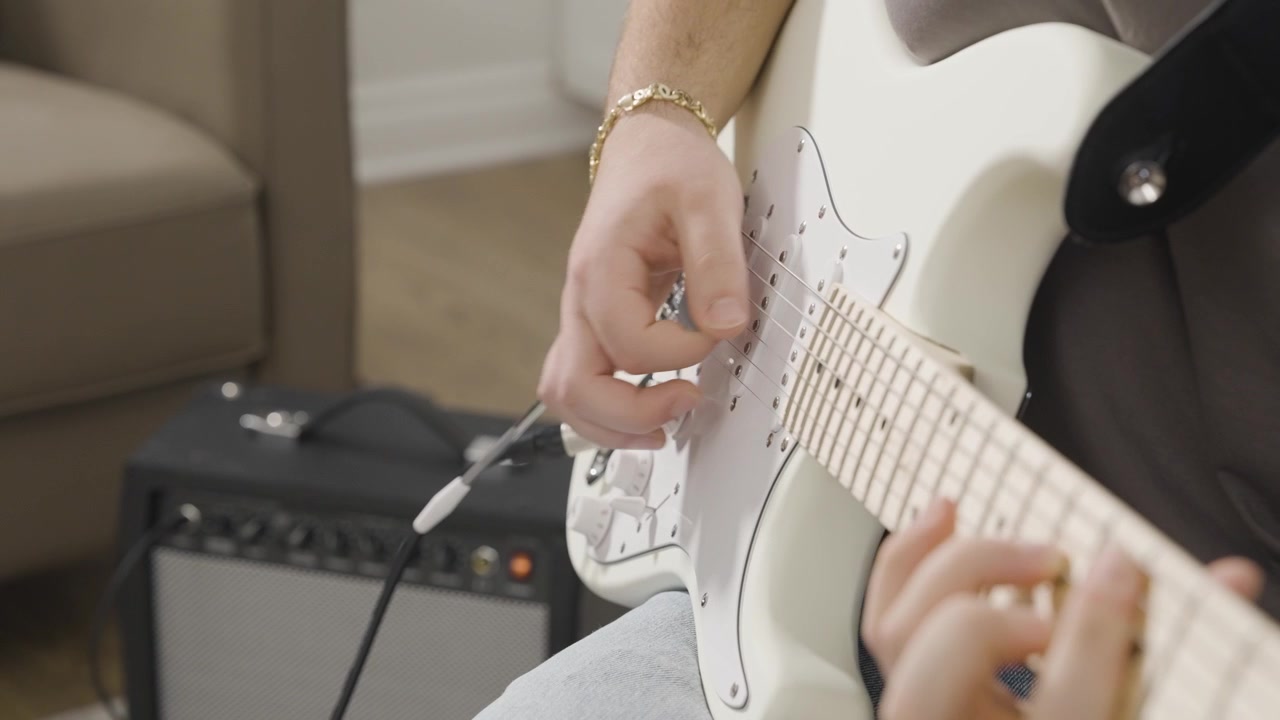 Dedilhando uma guitarra elétrica branca estilo Stratocaster com um pequeno amplificador ao fundo.