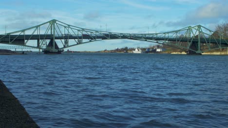 cars driving over the oskara kalpaka metal swing bridge at karosta, liepaja in sunny afternoon, camera tilts up, wide shot