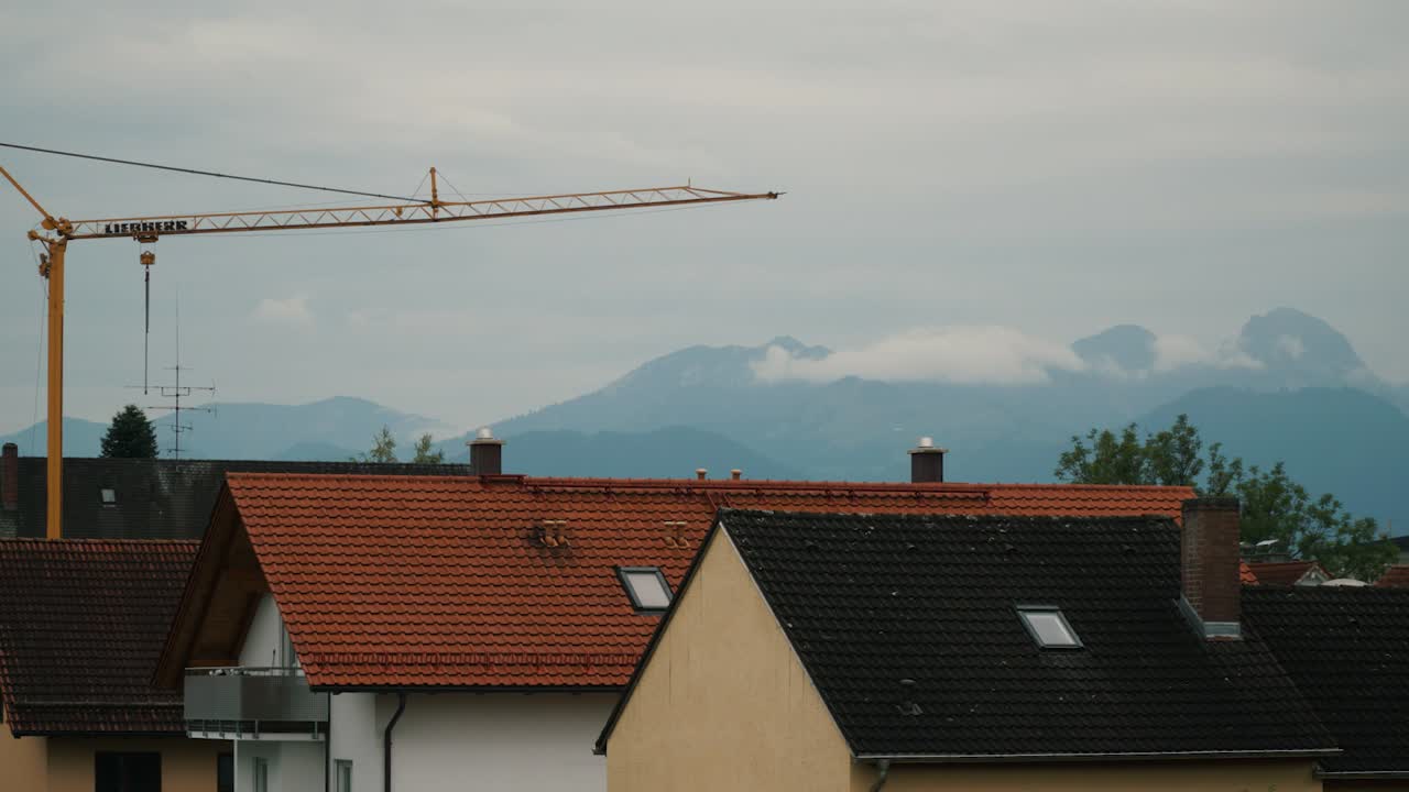Neighborhood house roof with construction and Bavarian alps landscape in the background, timelapse