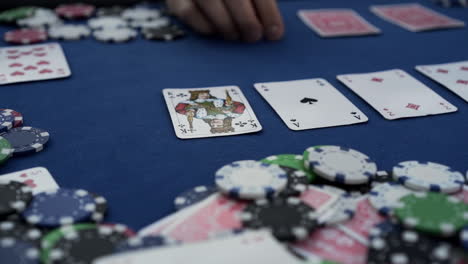 Partial-view-of-male-hand-with-casino-tokens,-playing-cards-on-blue-background,-Close-up-shot