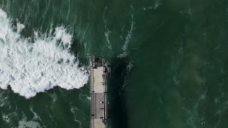 Large-waves-crashing-under-a-concrete-walking-platform-with-people-sightseeing