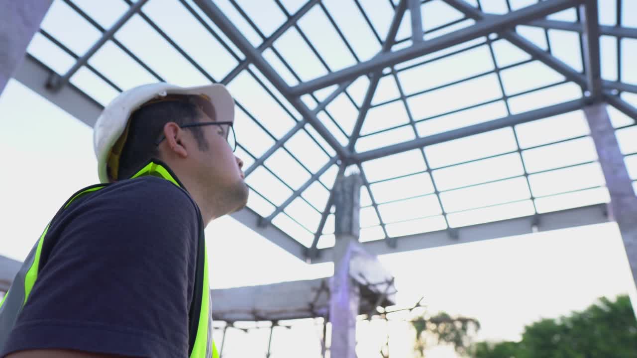un técnico ingeniero utiliza un papel de planos observando la estructura de techo de acero de inspección en el sitio de construcción de la casa.