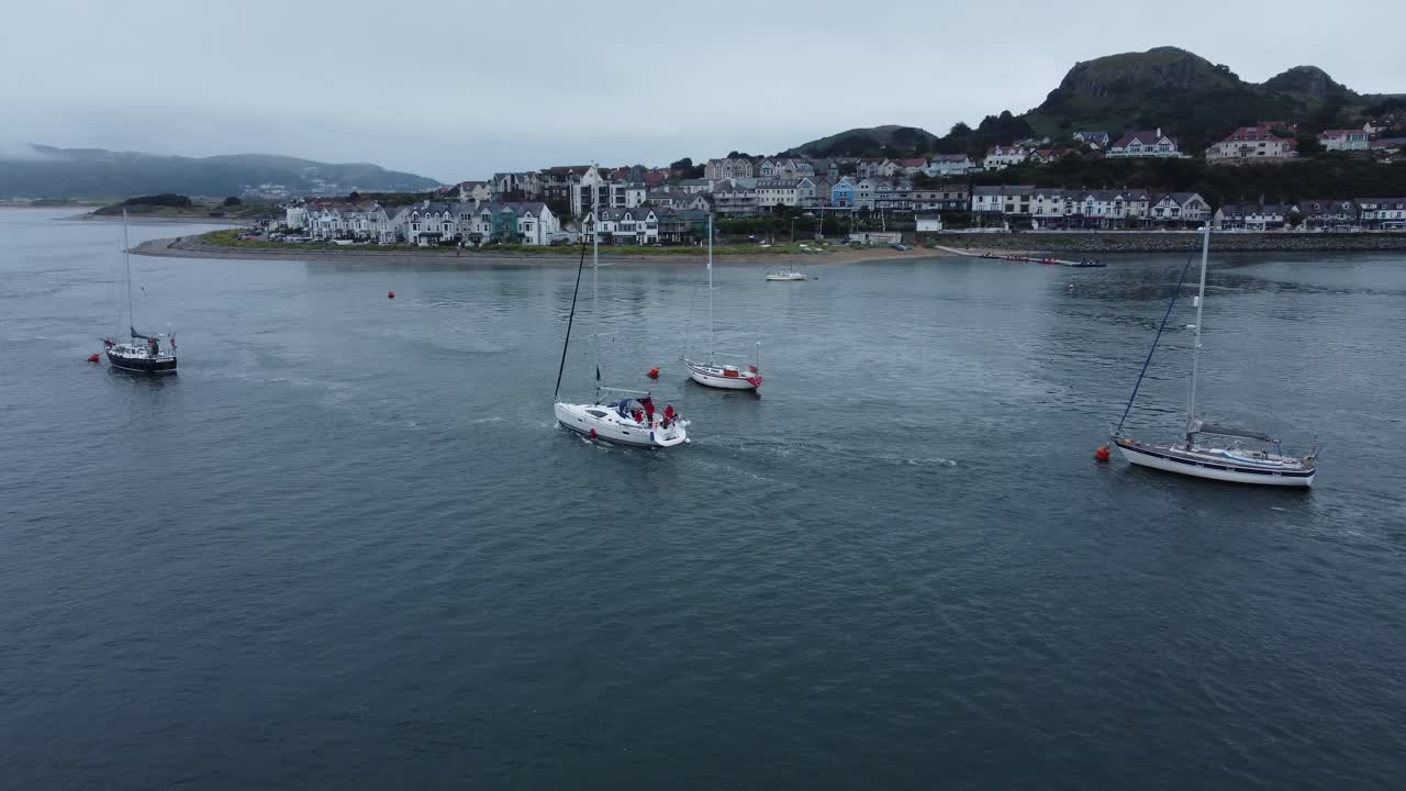 siga la vista aérea detrás del yate navegando junto al mar, ciudad galesa de montaña, río tranquilo, estuario de conwy