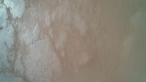 drone flight looking down and passing over masted sailing ship which is moored in mud flats during low tide. dolly shot forward.