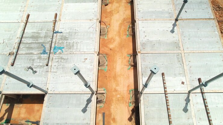 Symmetrische Drohnenaufnahme aus der Vogelperspektive, die vorwärts fliegt und sich über einer Baustelle für ein Geschäftsgebäude nach unten neigt, zeigt Stahlsäulen, Betondecken und Fundamente.
