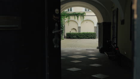 large historic doors open into a hidden courtyard in ljubljana, offering a peek through a tunnel-like passage into the heart of an old residential complex.