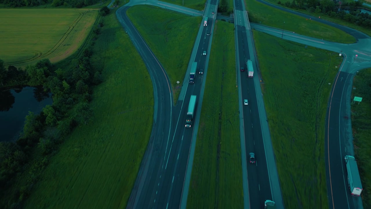 Rimorchi commerciali e autovetture che viaggiano lungo un corridoio interstatale. Uno svincolo a quadrifoglio rurale ripreso dall'alto nel tardo pomeriggio