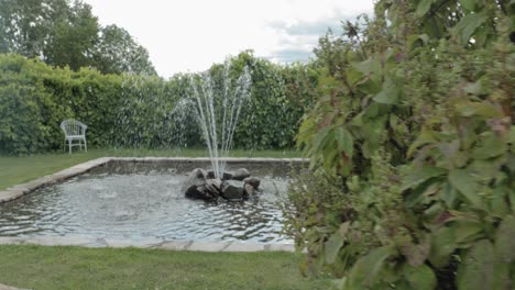 reveal of a gorgeous fountain feature from behind a bush on a gorgeously landscaped acreage