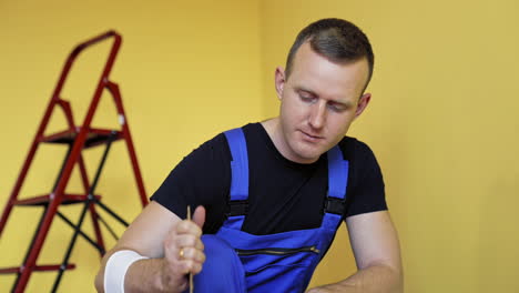 portrait of a worker preparing dye for renovation. craftsman in blue overalls mixing paint on the background of ladder in the room.
