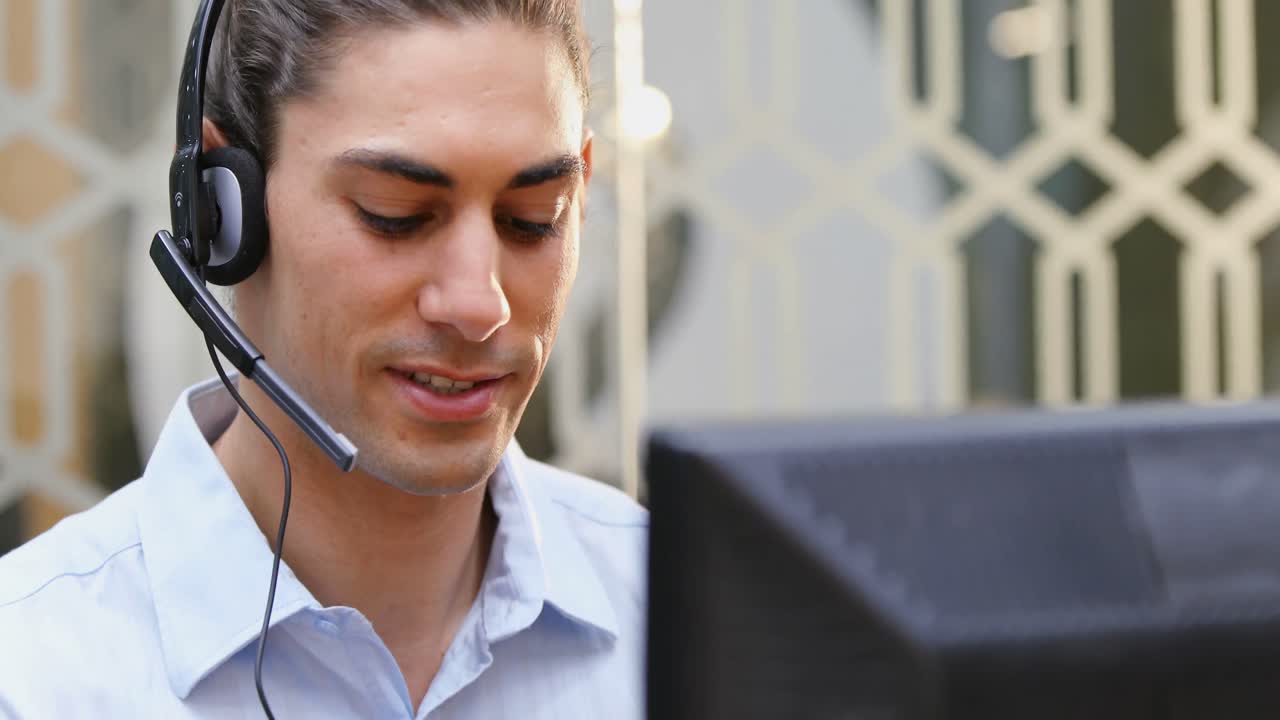 Smilende kundebehandler snakker i headset ved pulten 4k