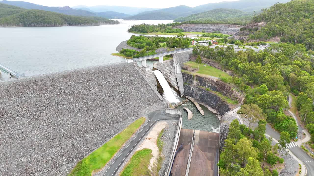 Water flows over dam surrounded by lush greenery