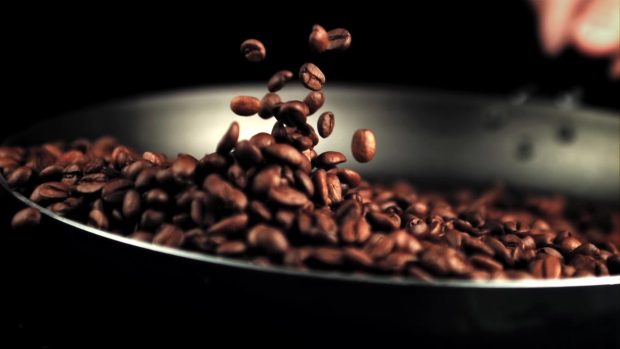Movimento rallentato di chicchi di caffè tostati che cadono in una padella