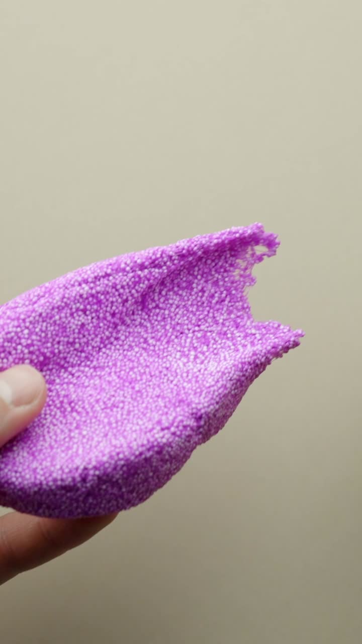 Vertical Close-up of a hand holding a round purple foam disc filled with tiny beads, showing its texture and lightweight design