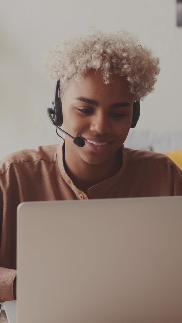 Afroamerikansk kvinde med headset til videoopkald via bærbar computer, vinker med hånden.