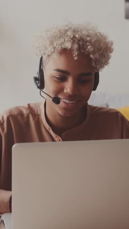 african american woman with headset for video calls via laptop waving hand
