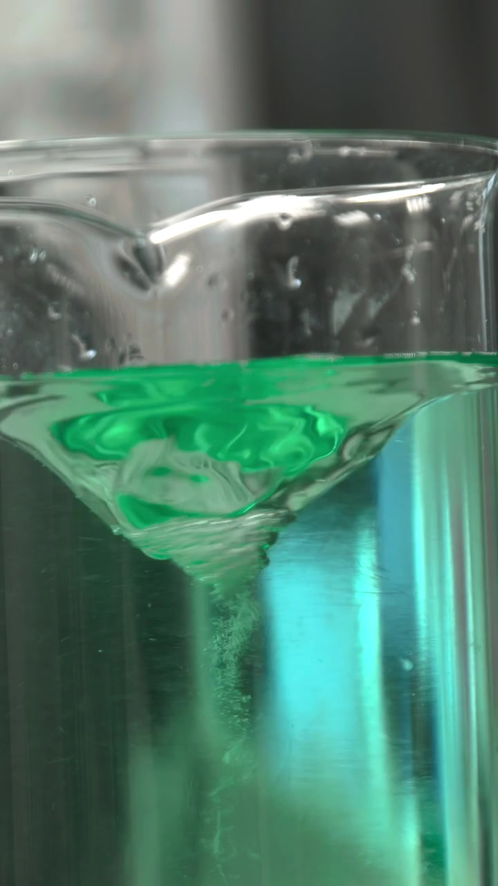 Primo piano di becher con vortice verde che si forma, retroilluminazione brillante che evidenzia il liquido verde acqua vivido che ruota