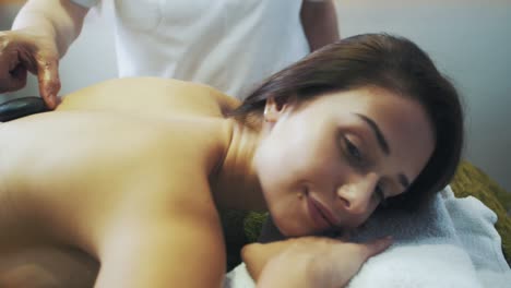 young girl lying on a massage table, masseur is putting hot stones on her back