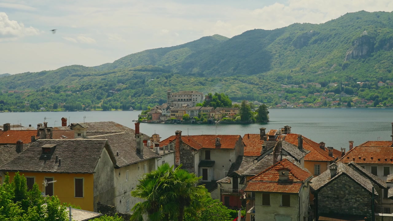 Orta Gölü'ndeki pitoresk Isola San Giulio'ya doğru turuncu çatılar üzerinden nefes kesen manzara, yemyeşil dağlarla çevrili. Açık bir yaz gününde güzel İtalyan göl kenarı manzarası.