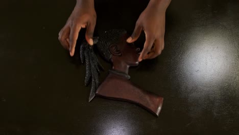 top down shot of an african american man's hands placing a female wooden african mask on a brown table