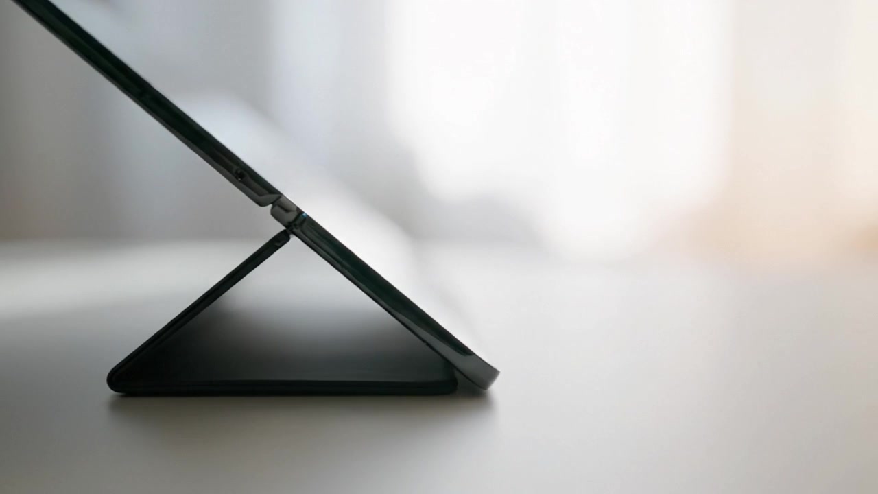 A sleek tablet propped at an angle on a smooth white surface, showcasing its modern design against a softly lit, blurred background that adds elegance.