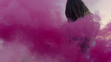 hermosa mujer agitando granada de humo rosa bailando en la playa temprano en la mañana celebrando la libertad creativa