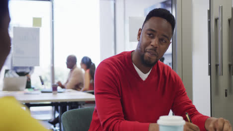 African-american-male-and-female-business-colleagues-talking-and-taking-notes-in-office