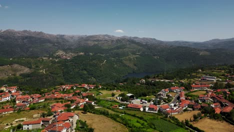 aerial - picturesque salamonde village with red rooftops, lush fields, and dramatic gerês mountain backdrop in portugal