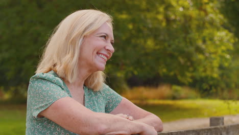 portrait of laughing mature or senior woman leaning on fence on walk in countryside