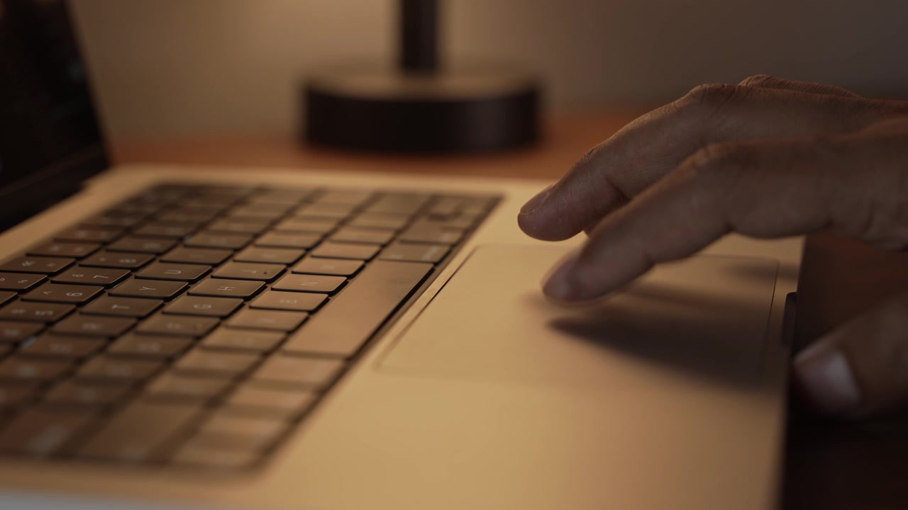 Hand Using Laptop Trackpad in Warm Cozy Lighted Room.