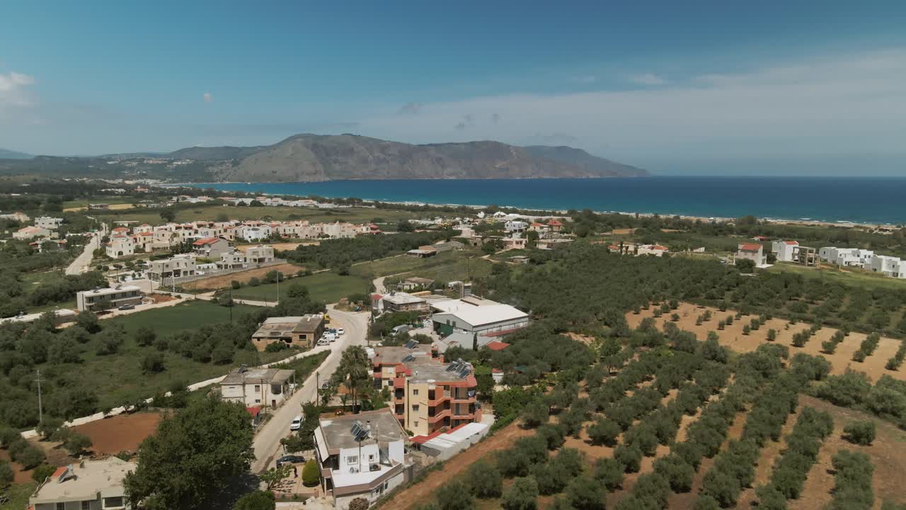 Drone view of coastal Crete with a rural village, green olive orchards and the blue Mediterranean Sea stretching across the horizon near Asprouliani